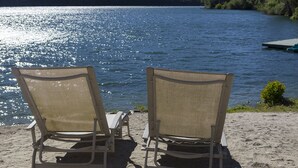 Två strandstolar placerade så att de vetter mot en sjö, med en brygga i bakgrunden.