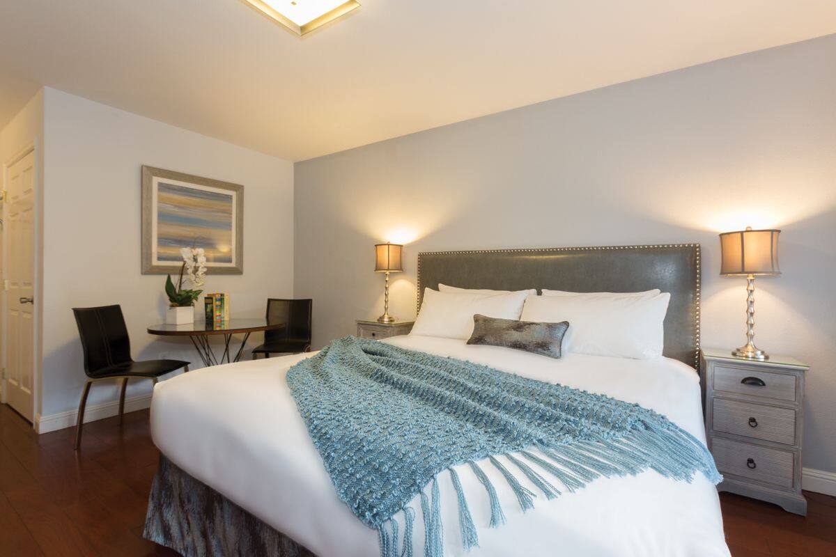 A neatly arranged bedroom with a large bed, bedside lamps, a desk with a chair, and a framed picture on the wall.