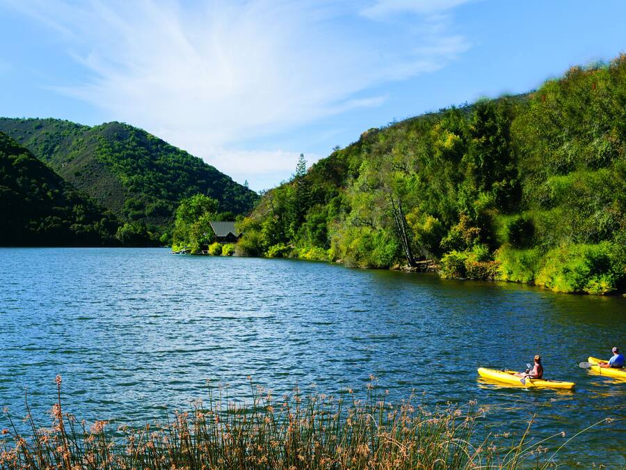 Um lago calmo com caiaques, cercado por colinas verdejantes.