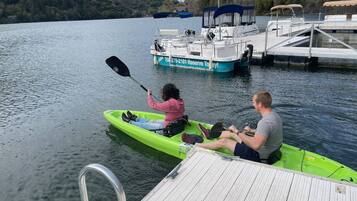 A man and a woman kayaking on a green kayak on a calm lake with a dock and a boat in the background.