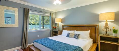 A neatly arranged bedroom with a large bed, bedside lamps, a nightstand, a window with curtains, and a ceiling fan.