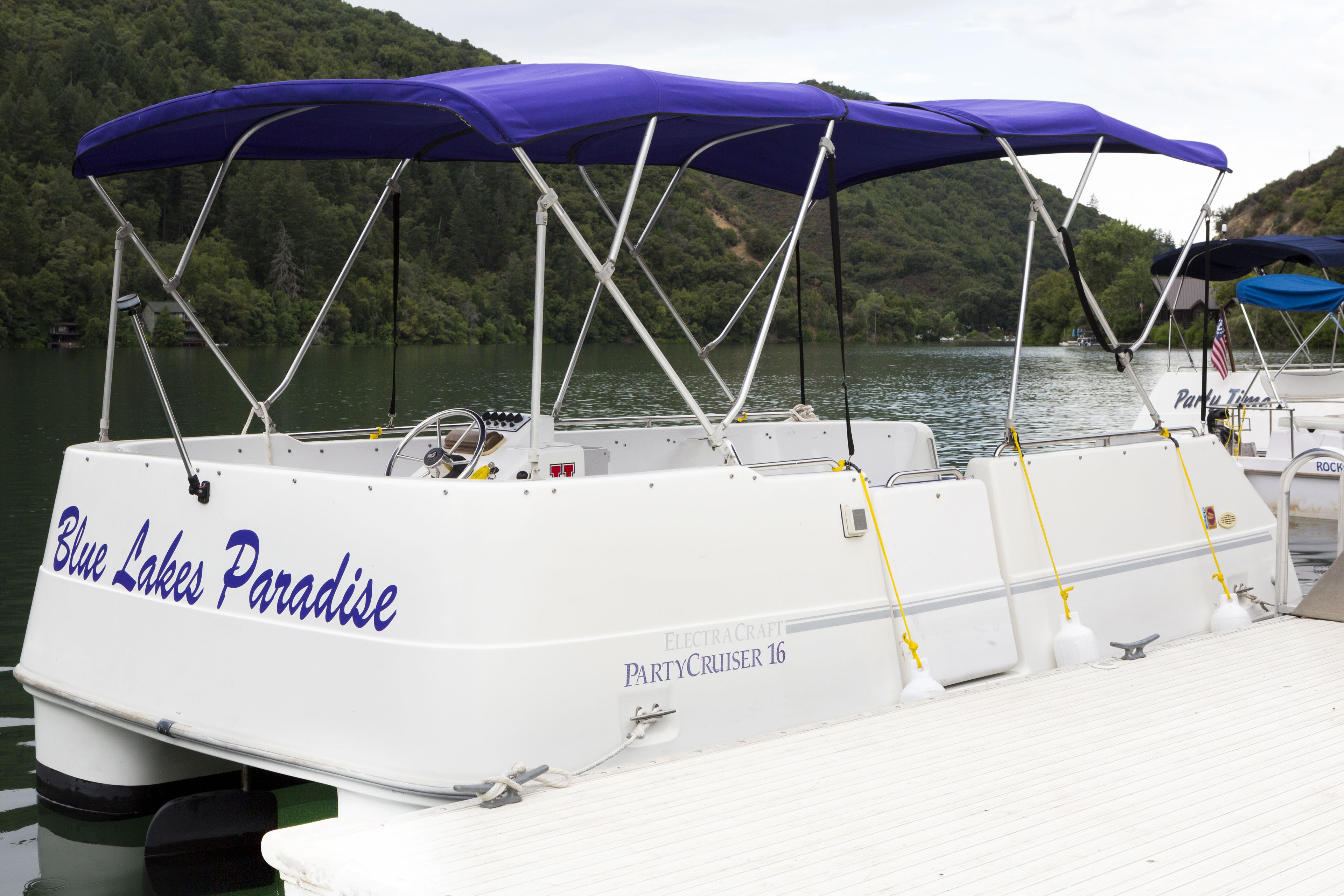 Una barca chiamata "Blue Lakes Paradise" con una zona coperta sul ponte, uno scafo bianco e l'etichetta "PartyCruiser 16".