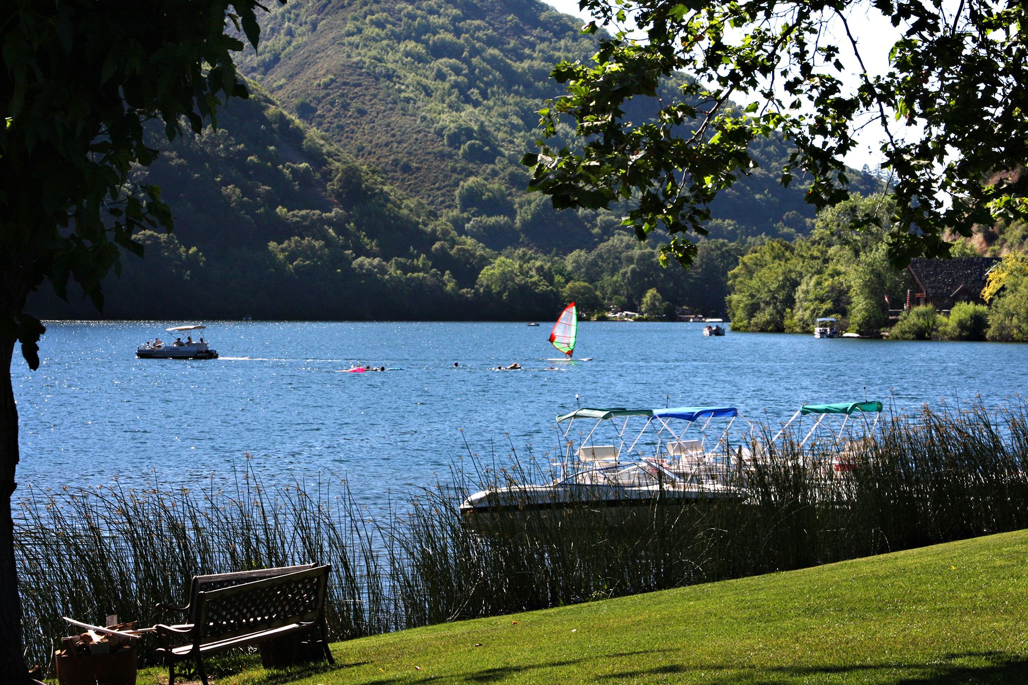 A lake with boats, a windsurfing board, and a row of beach chairs.