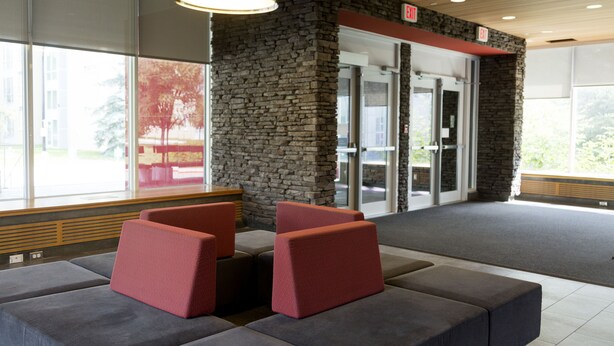 A modern lobby with stone walls, a reception desk, and seating areas. - University of Calgary Accommodations & Events (Calgary)