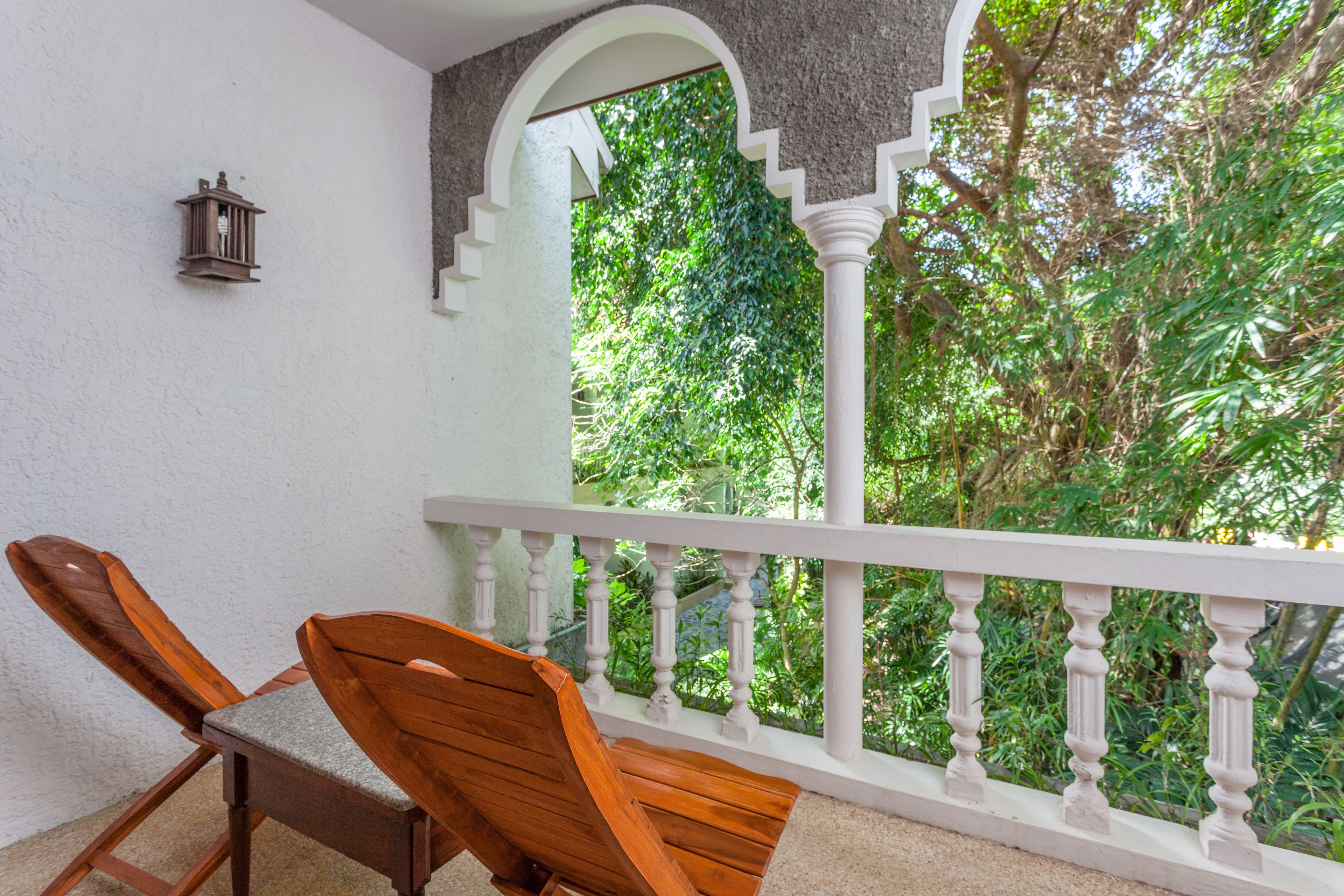 A balcony with two wooden chairs, a white railing, and a view of lush greenery.