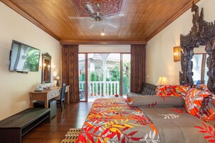 Un dormitorio con cama, escritorio, silla, televisor y balcón con vistas a zonas verdes.