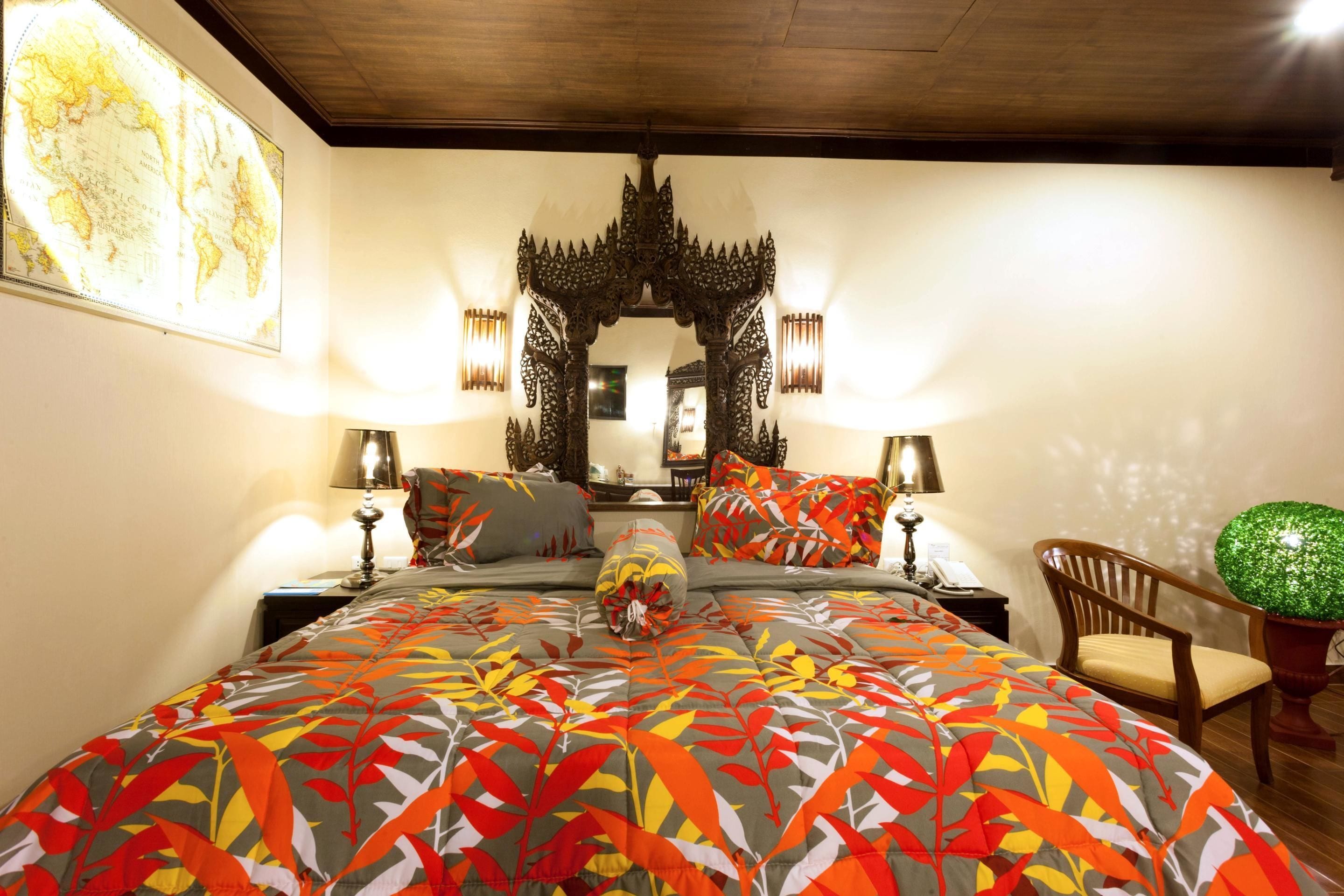 A bedroom with a large bed, decorative pillows, a wooden chair, a globe map, and a mirror with ornate carvings.