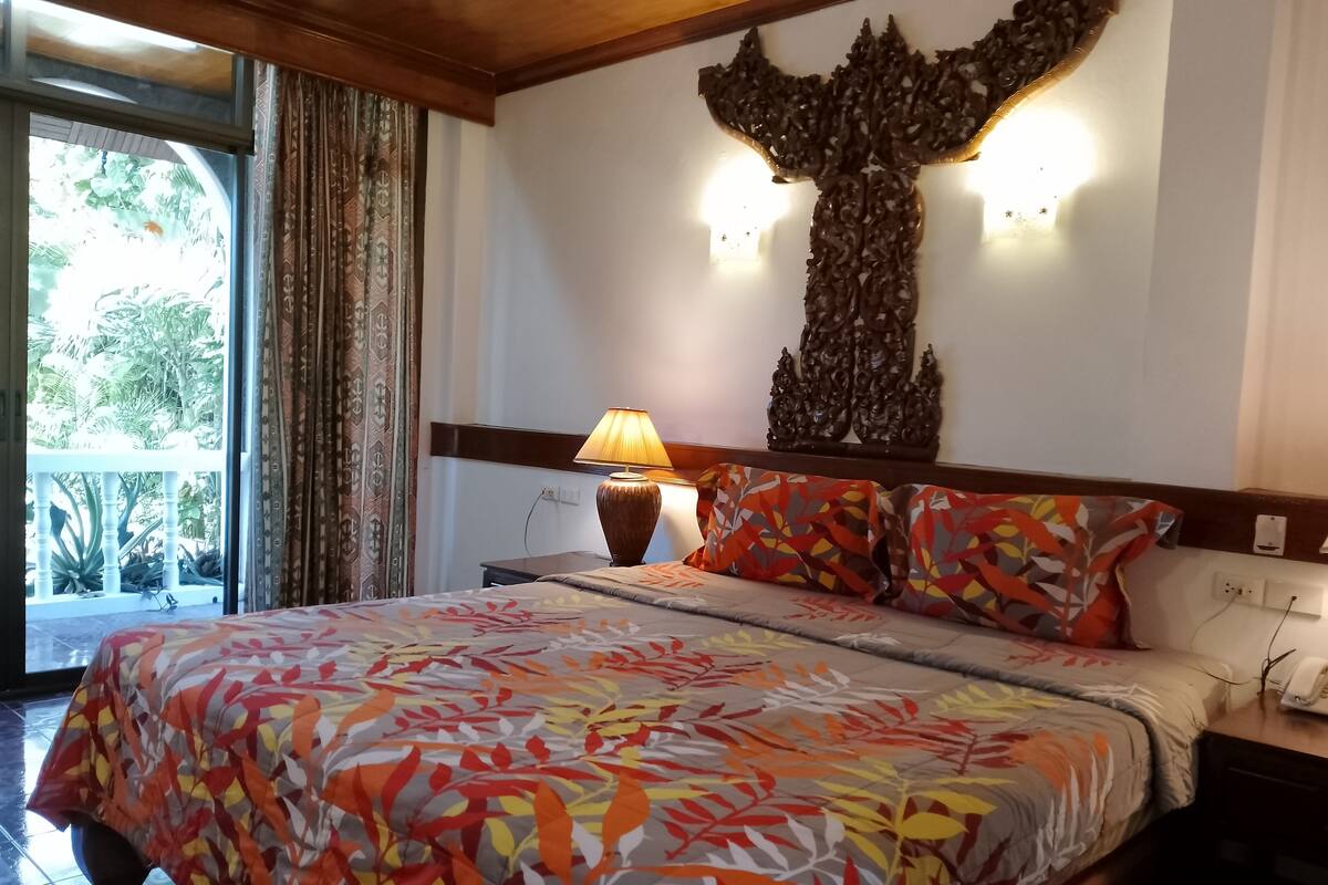 A hotel room with a bed, a nightstand, a lamp, and a wall-mounted light fixture.