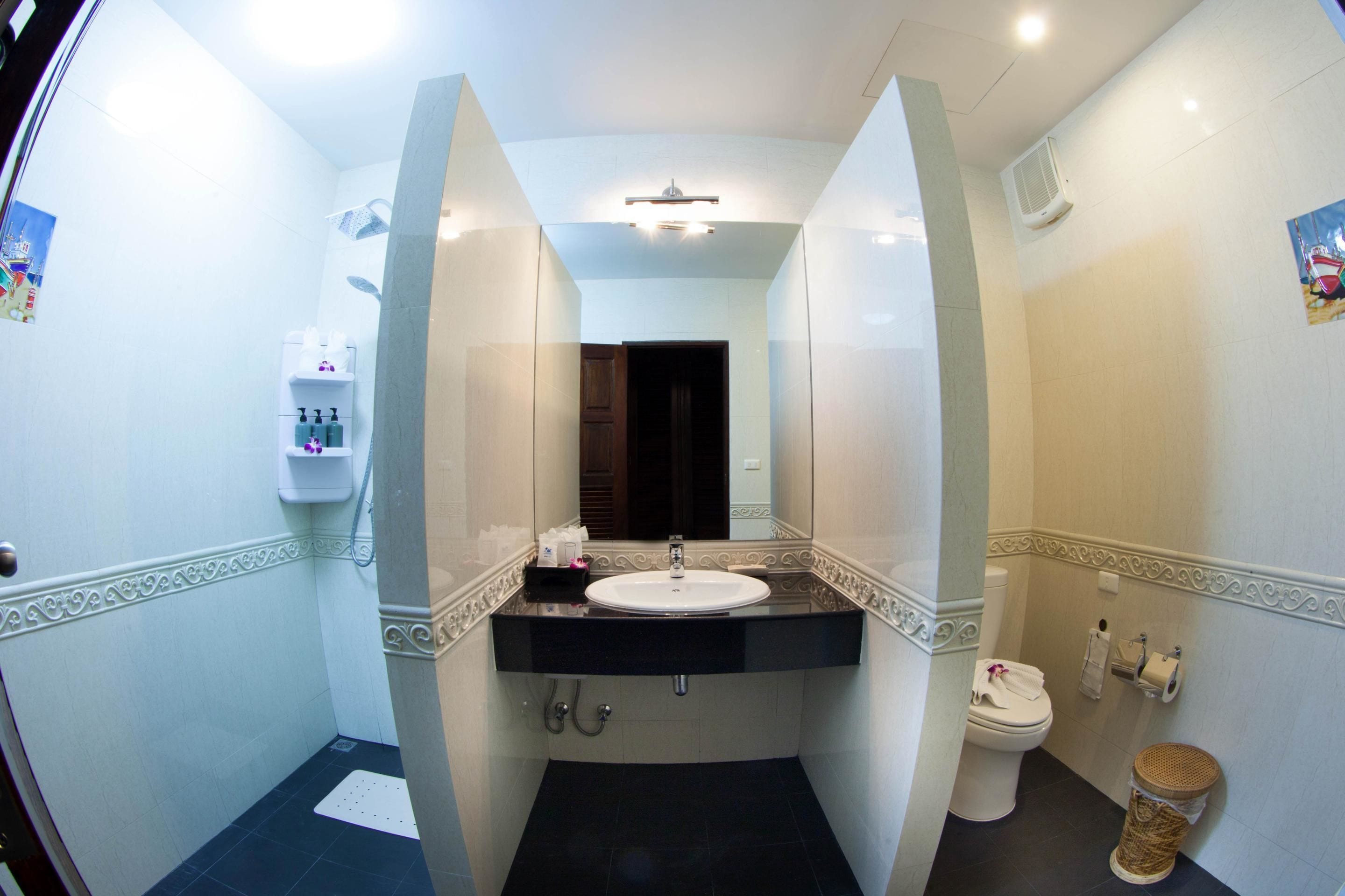 Un baño con lavamanos blanco, suelo de baldosas oscuras, un espejo y un inodoro.