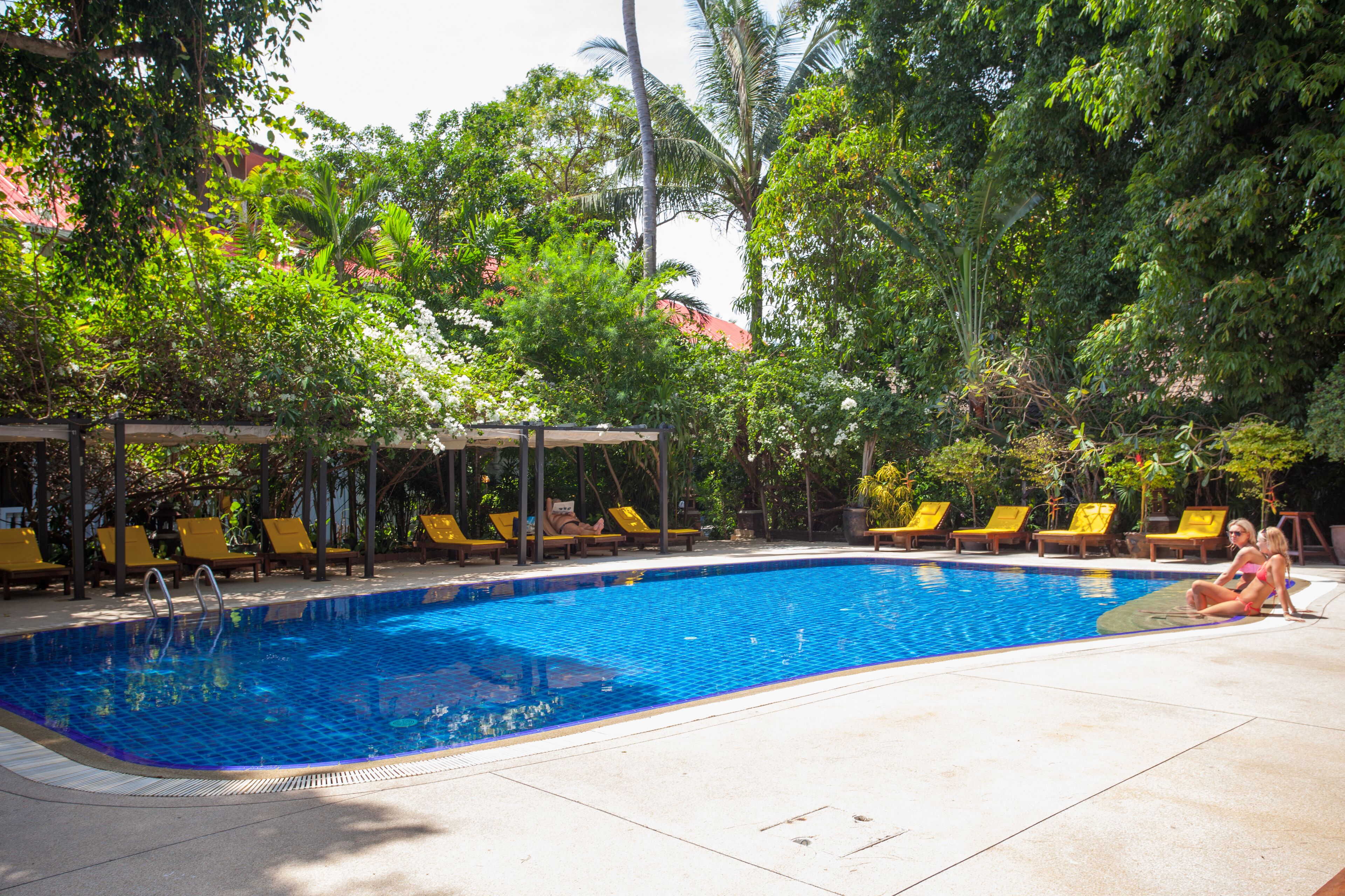 A swimming pool with lounge chairs and a covered seating area surrounded by trees.