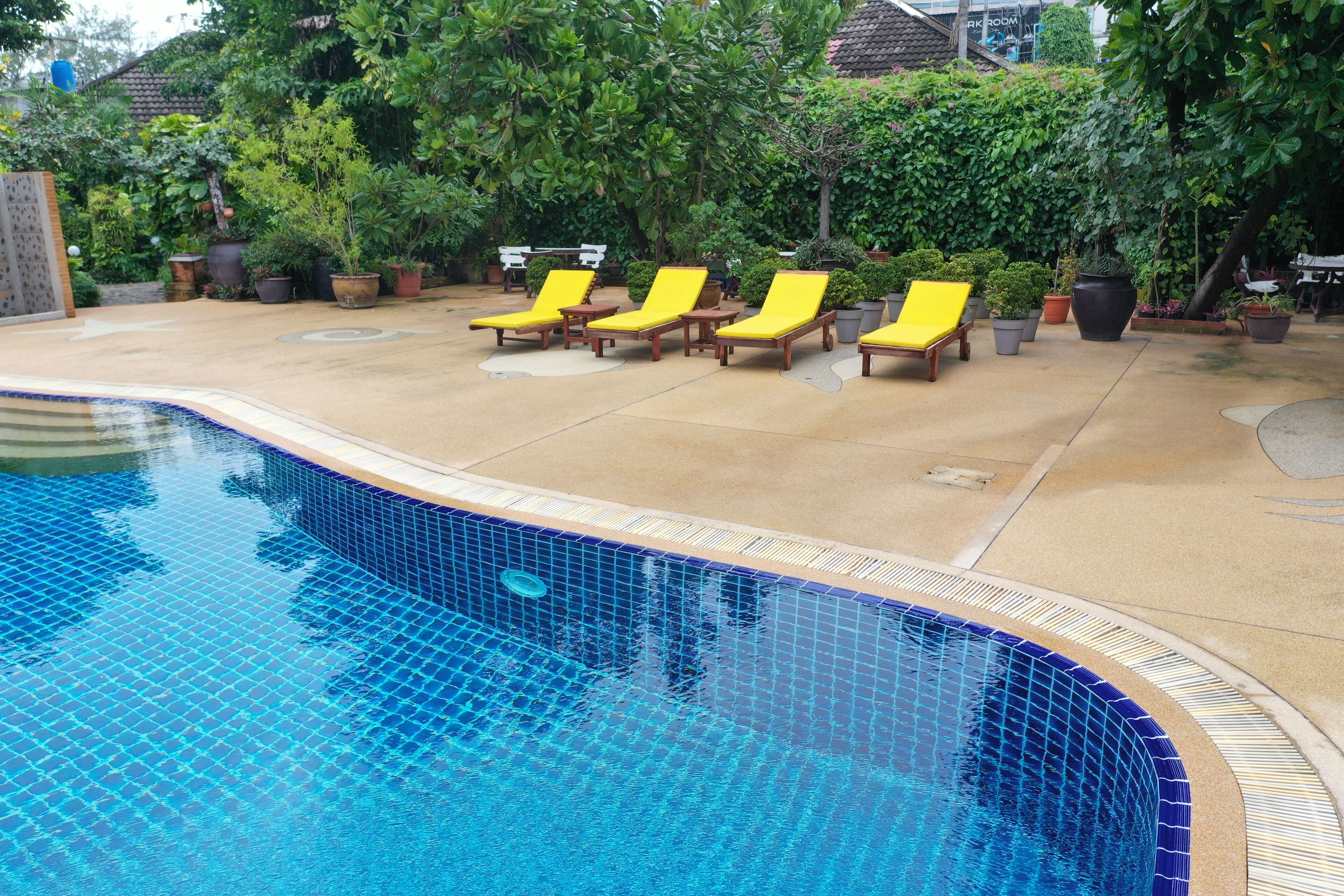 A swimming pool with tiled edges and a tiled deck area with yellow lounge chairs.