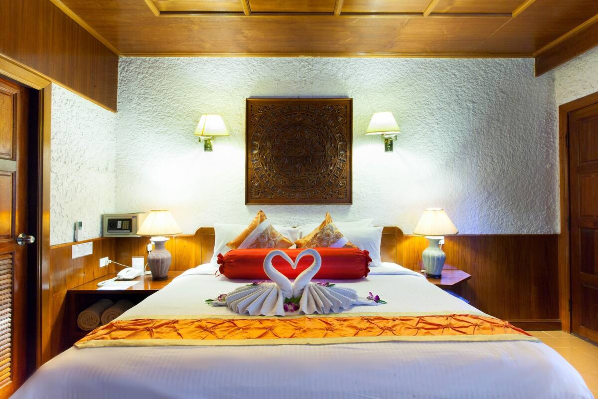 A hotel room with a neatly made bed, two wall-mounted lamps, a decorative wall piece, and a wooden ceiling.