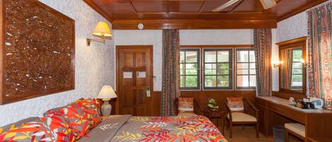 A hotel room with a bed, desk, chairs, and a window with curtains.
