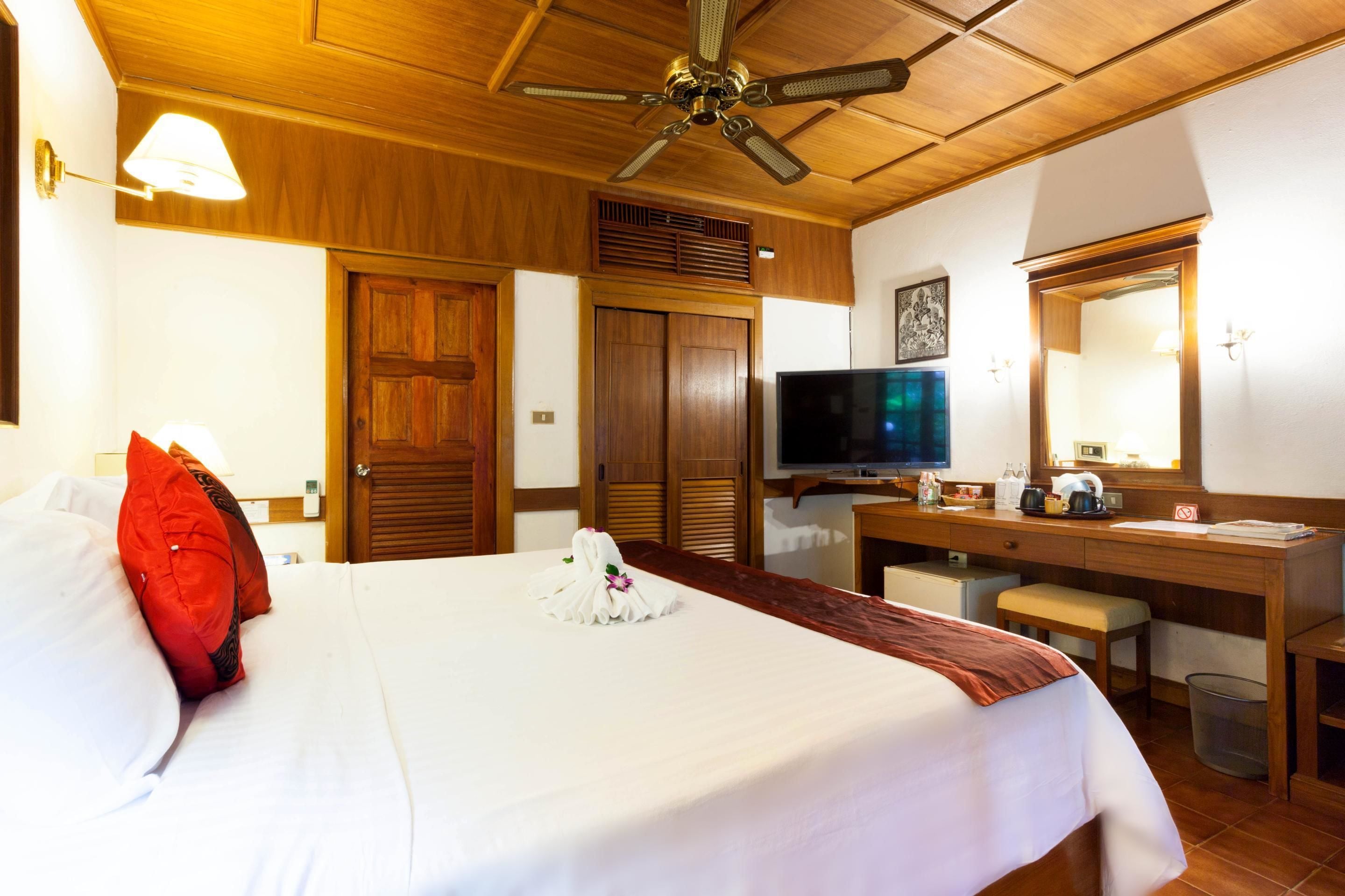 Una habitación de hotel con cama, escritorio, televisor y ventilador de techo.