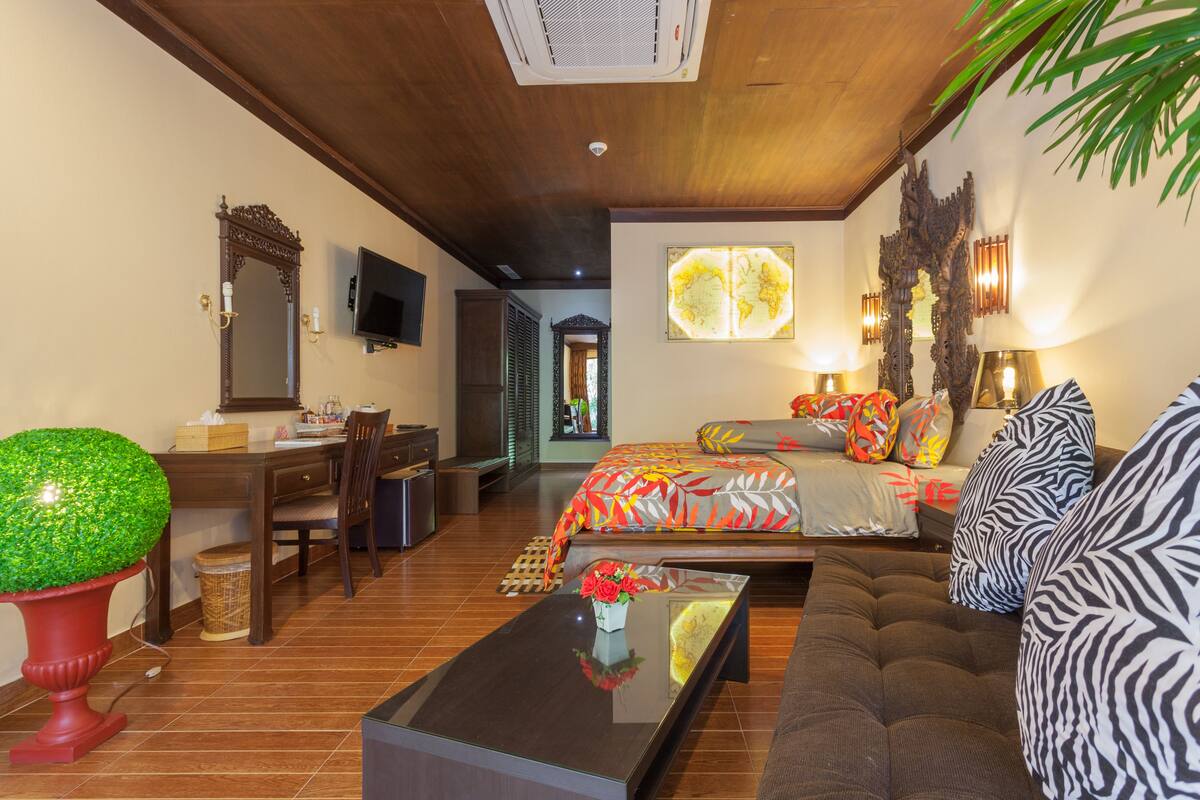 A well-lit room with a bed, a sofa, a dining table, and a TV.
