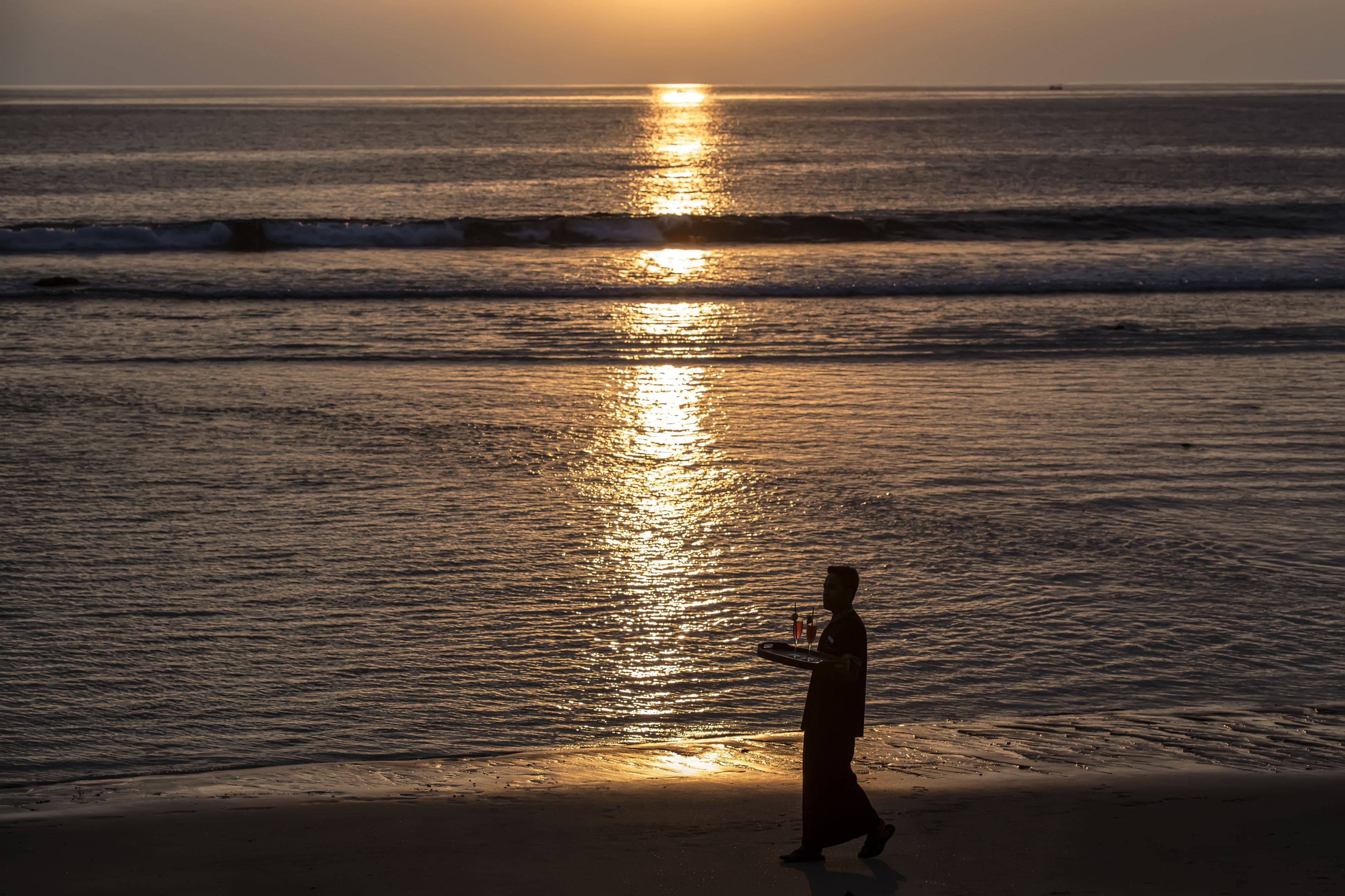 Una persona caminando por la playa, con el sol reflejándose en el agua.