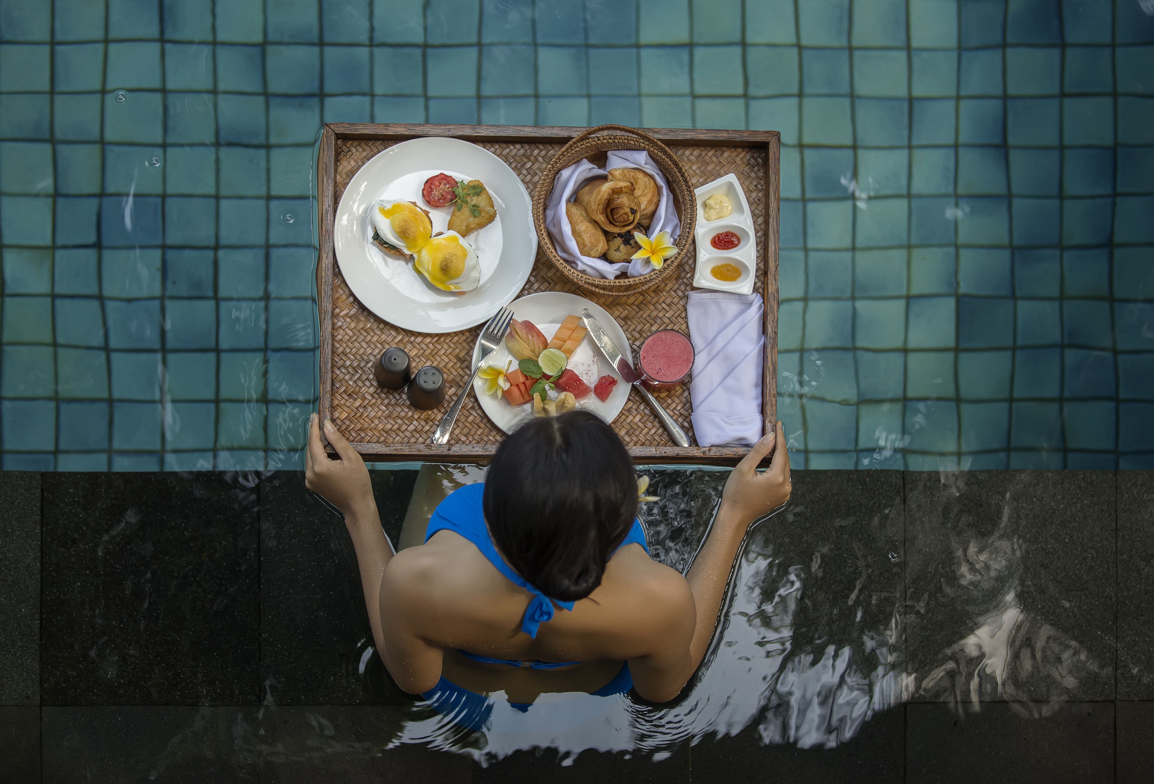 A person holding a tray with various food items over a pool.