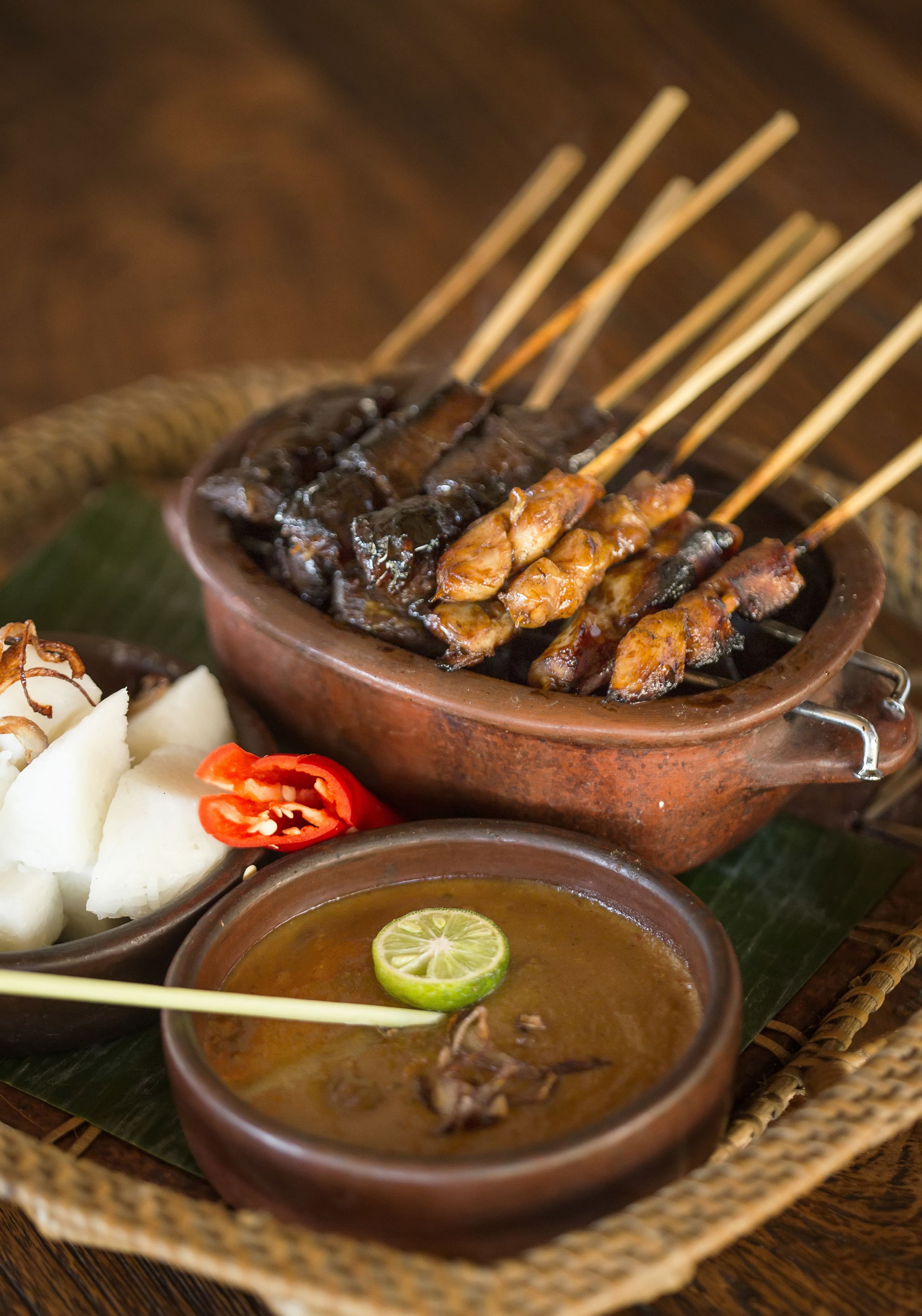A traditional dish with skewered meat, a bowl of soup, and sliced vegetables.