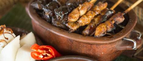 A traditional dish with skewered meat, a bowl of soup, and sliced vegetables.