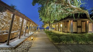 A wooden pathway leading to a building with bamboo walls and a stone wall on the left. - Jeeva Klui Resort (Senggigi)