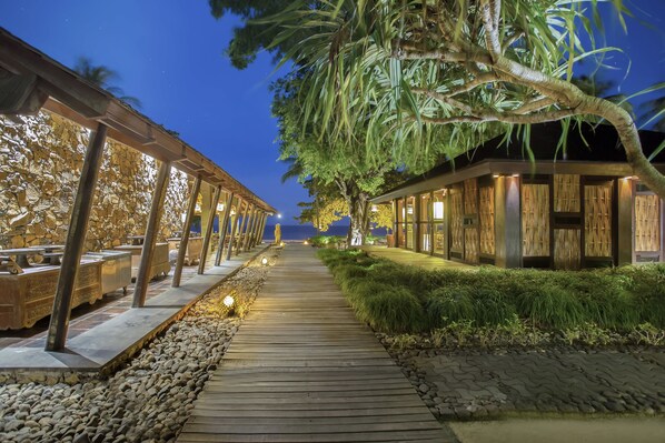 A wooden pathway leading to a building with bamboo walls and a stone wall on the left. - Jeeva Klui Resort (Senggigi)
