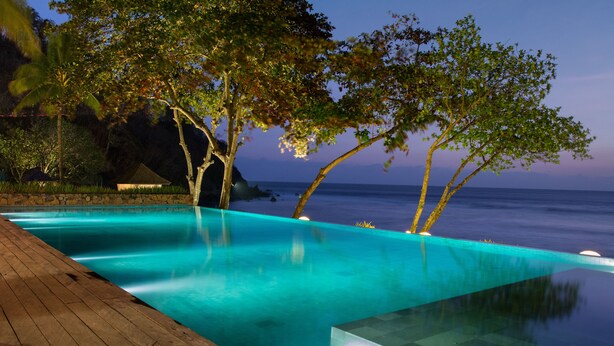 A serene infinity pool with a wooden deck, surrounded by lush greenery and overlooking the ocean. - Jeeva Klui Resort (Senggigi)