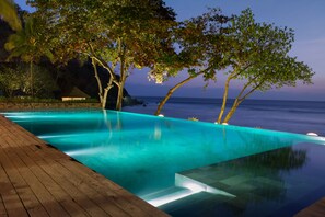 A serene infinity pool with a wooden deck, surrounded by lush greenery and overlooking the ocean. - Jeeva Klui Resort (Senggigi)
