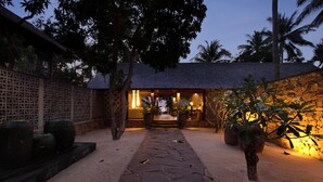 A stone pathway leading to a building with a thatched roof, surrounded by trees and plants. - Jeeva Klui Resort (Senggigi)