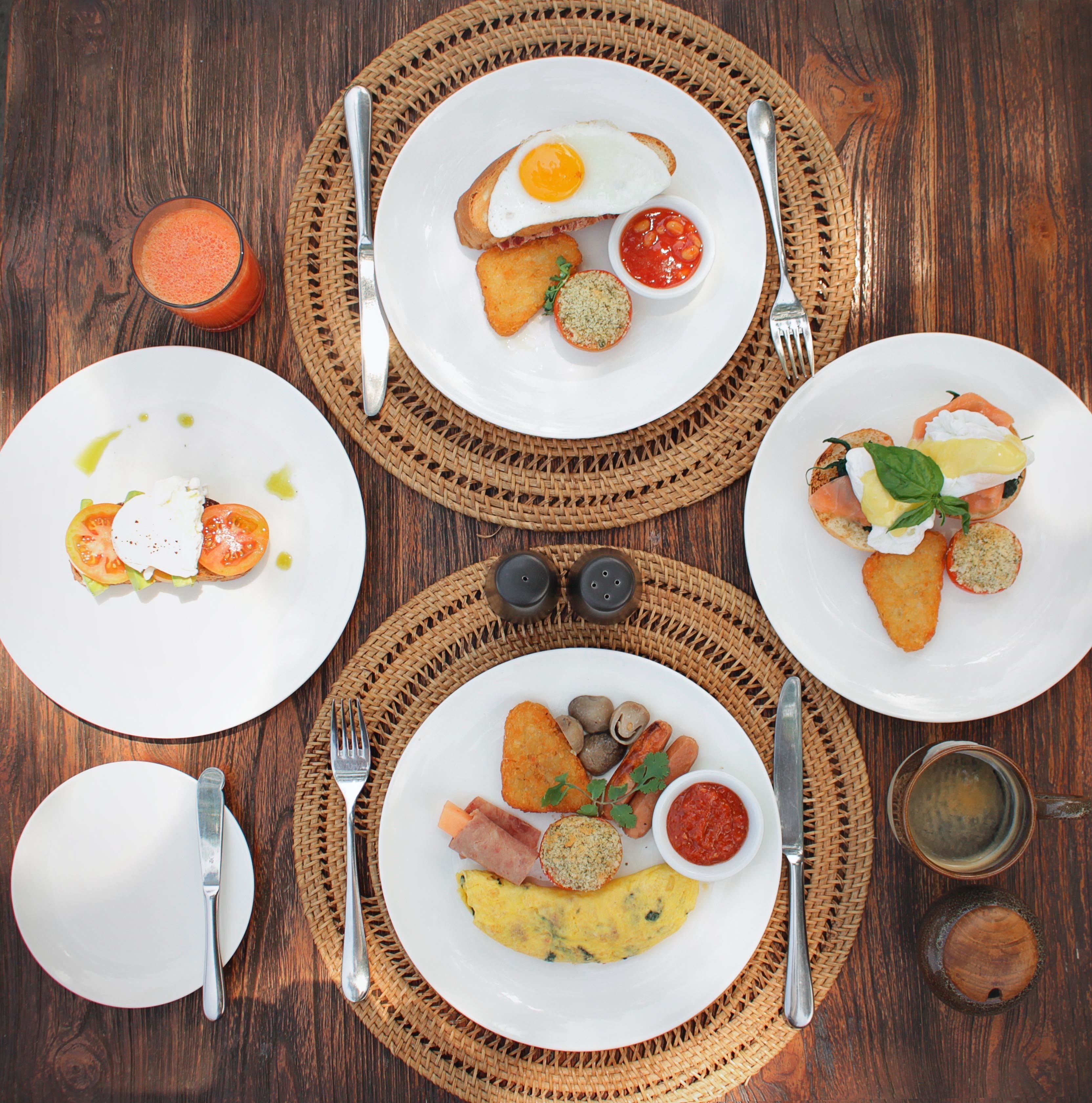 Une table en bois dressée pour le petit-déjeuner, avec des assiettes d’œufs, des toasts et divers accompagnements.