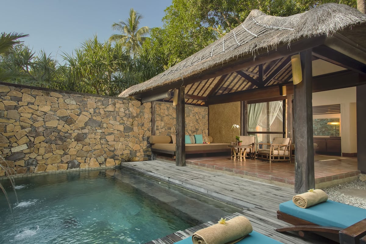 A pool area with a stone wall, wooden deck, and lounge chairs.