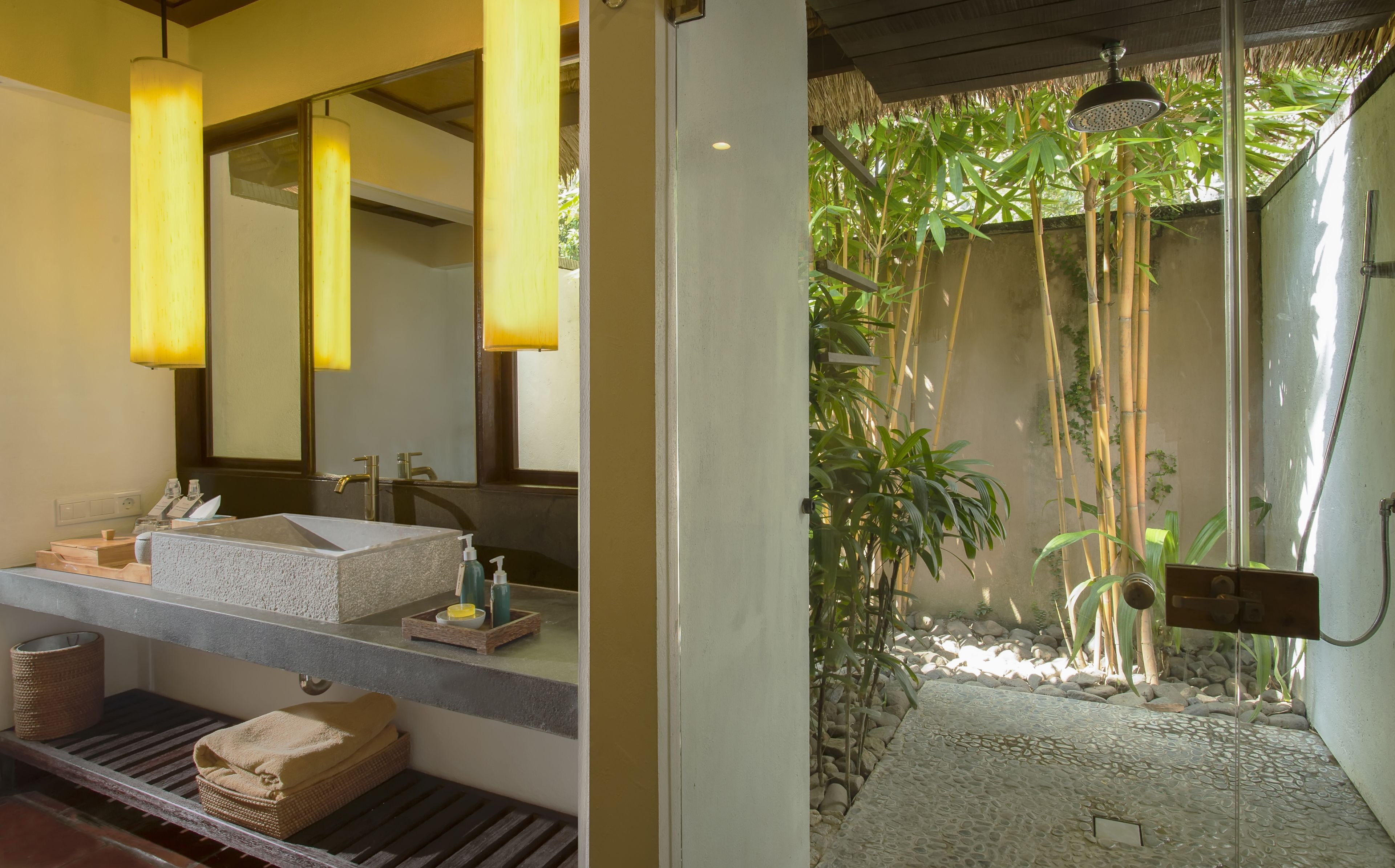 A bathroom with a large mirror, two sinks, and a shower area with bamboo plants.