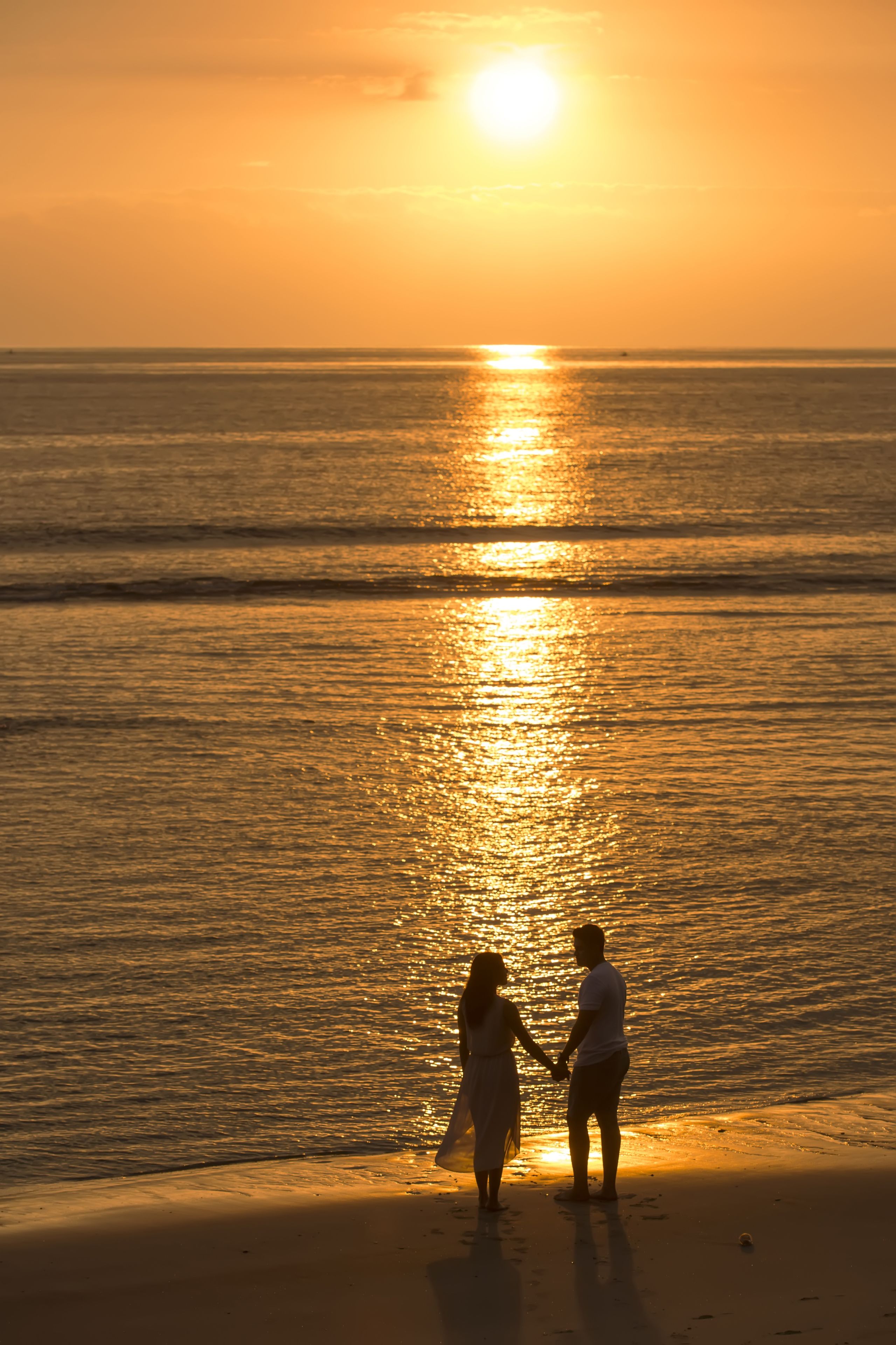 A couple holding hands on a beach at sunset.