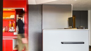 A modern interior with a red counter, a white reception desk, and a textured grey wall. - hotelF1 Nemours (Nemours)