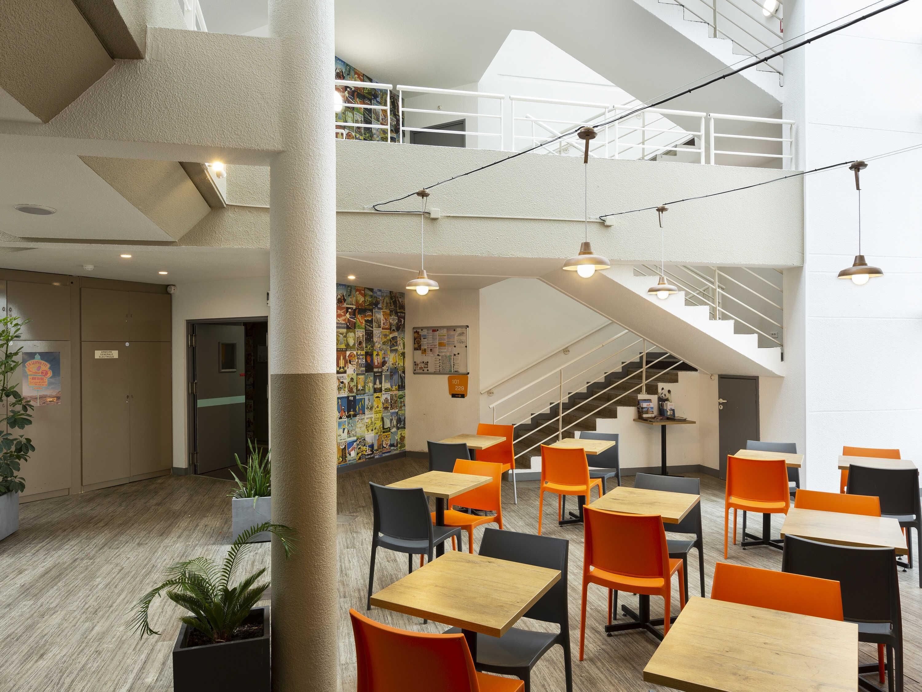 Um espaço moderno e interno com várias mesas e cadeiras, uma escada e um mural na parede.