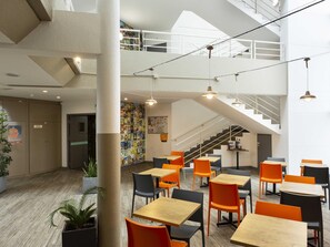 A modern indoor space with multiple tables and chairs, a staircase, and a mural on the wall.