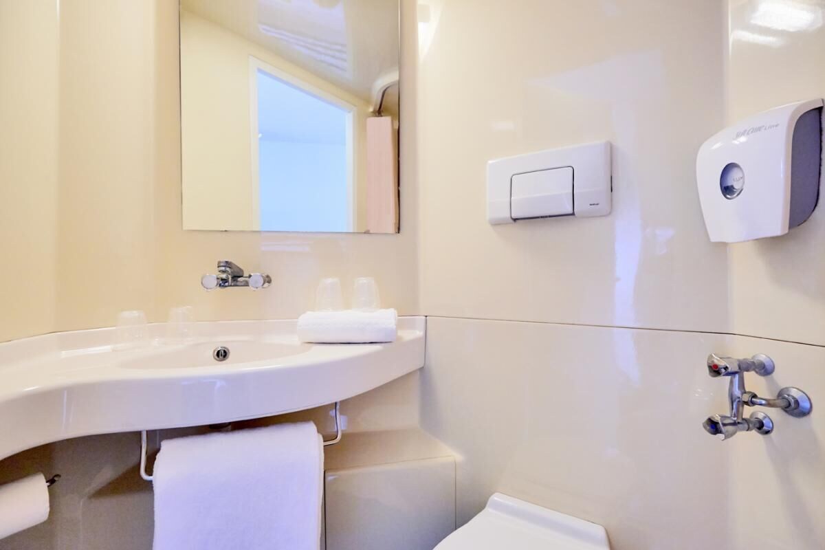 A modern bathroom with a large sink, a mirror, a towel rack, a soap dispenser, and a toilet.