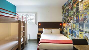 A dorm-style room with bunk beds, a single bed, a desk, and a wall adorned with travel posters.