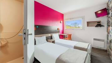 A hotel room with two beds, a desk, a chair, a TV, and a window with a view.