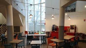 A modern cafe with wooden tables and chairs, a coffee machine, and a large window with a view of trees. - hotelF1 Nemours (Nemours)