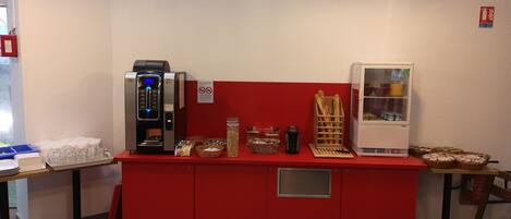 Una kitchenette con cafetera, refrigerador y diferentes alimentos sobre una encimera roja.