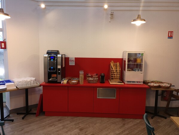 A kitchenette with a coffee machine, a refrigerator, and various food items on a red counter.