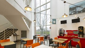 A modern café with wooden tables and orange chairs, large windows, and a staircase. - hotelF1 Nemours (Nemours)