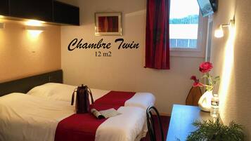 A twin room with a bed, a desk, a TV, a window with curtains, and a wall-mounted sign indicating the room size.