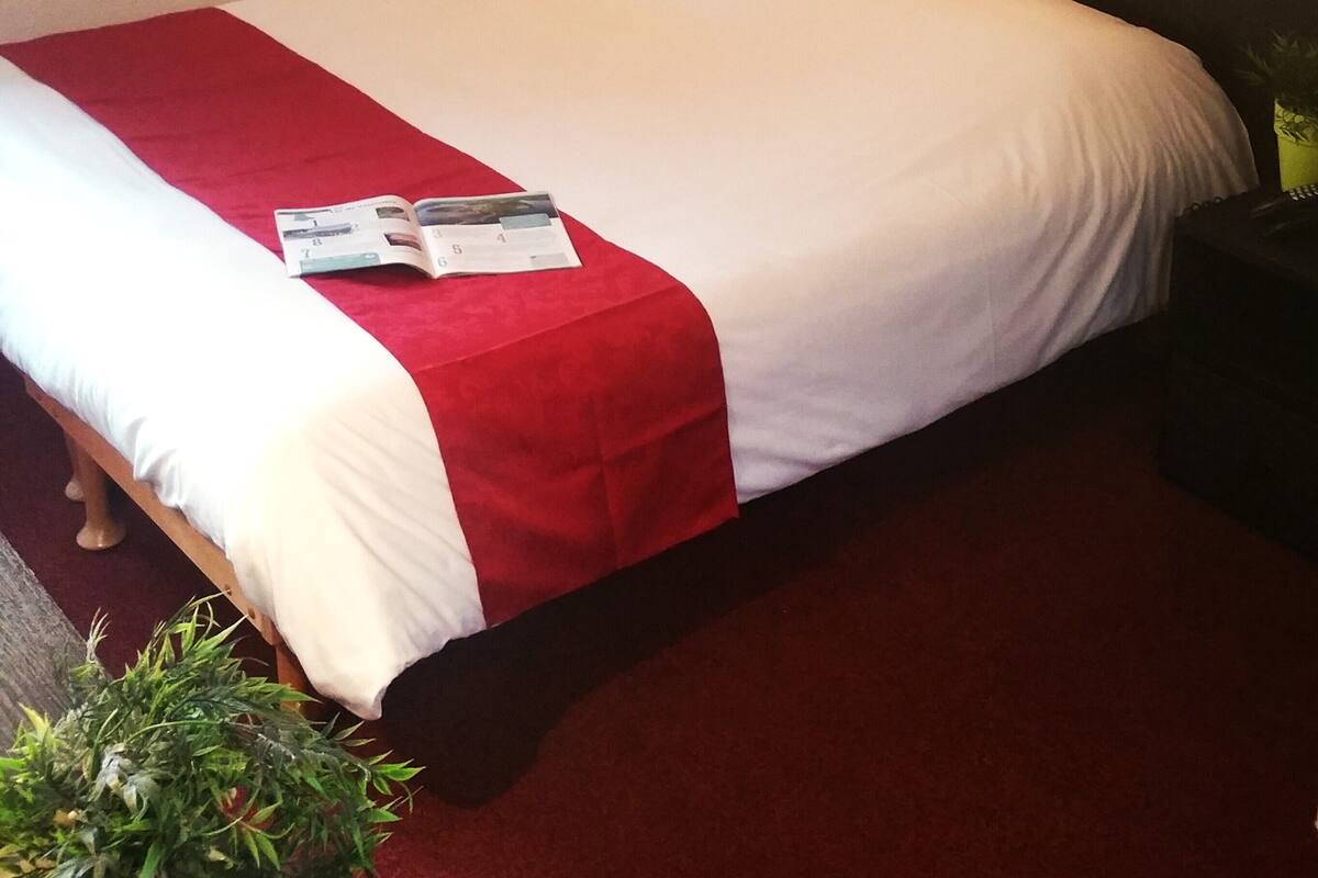 A neatly made bed with a red and white bedspread, a small bedside table with a lamp, and a framed picture on the wall.