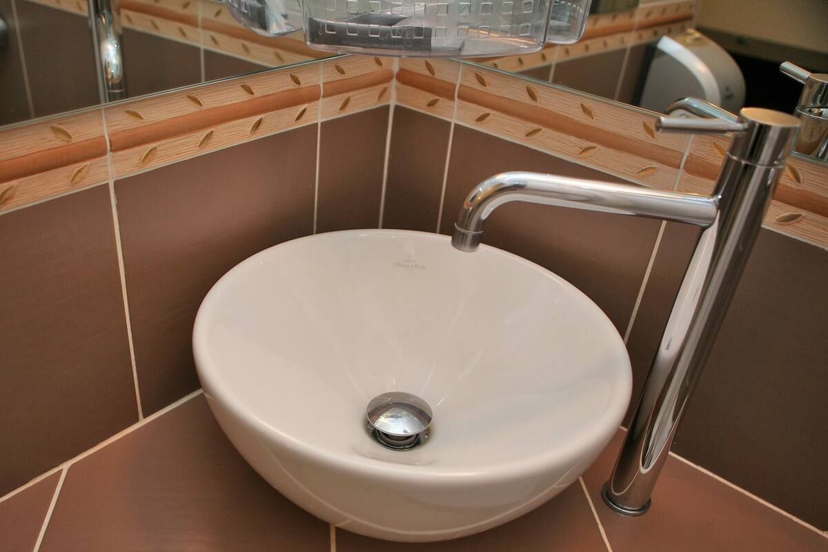 A bathroom with a white sink, chrome faucet, and brown tiled walls.