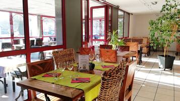 A restaurant with wooden tables and chairs, large windows, and potted plants.