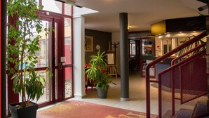 A hotel lobby with a reception desk, a staircase, and potted plants. - Hôtel du Parc (Limoges)
