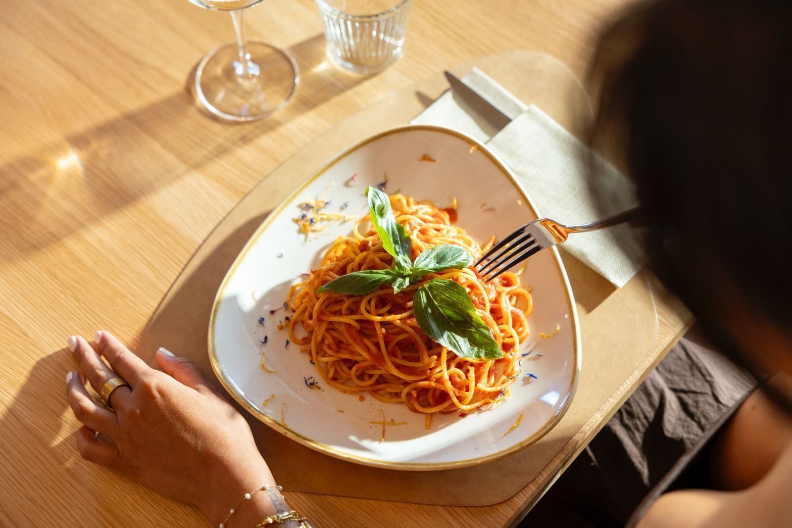 Een bord spaghetti met basilicum, een vork en een servetje op een houten tafel.