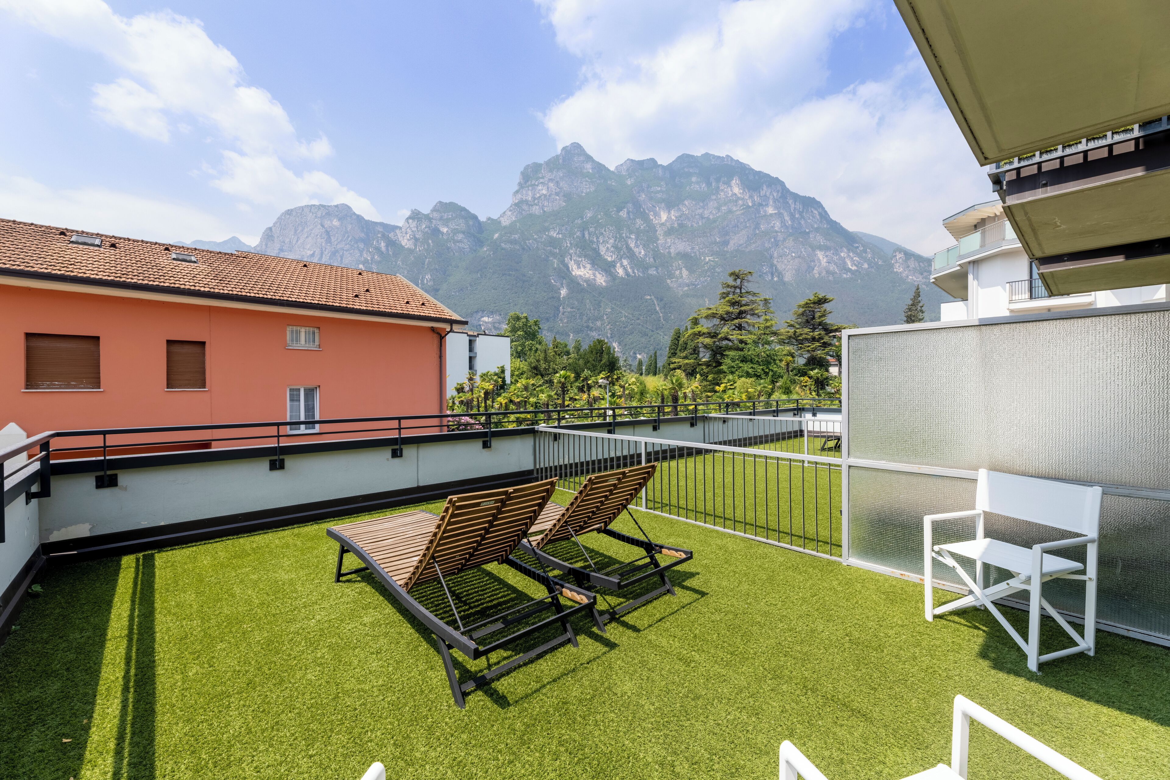 A rooftop terrace with artificial grass, two lounge chairs, a white chair, and a mountain backdrop.