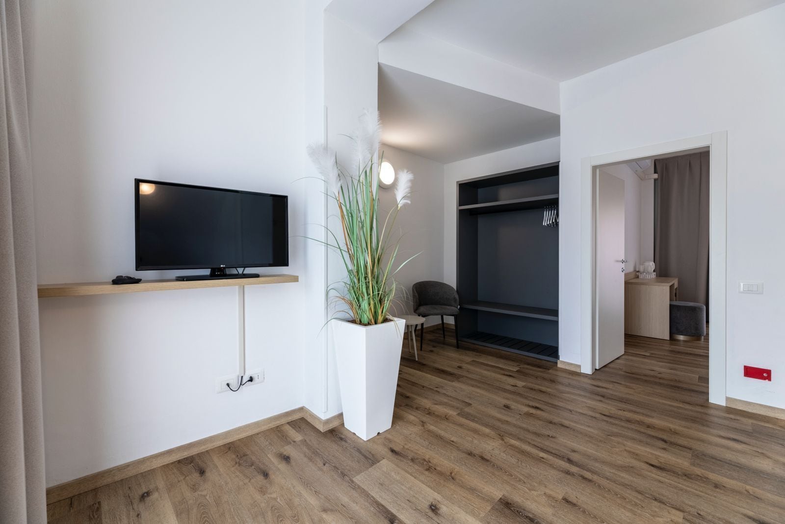 Un salon moderne avec un téléviseur à écran plat, une plante en pot, un fauteuil gris et une armoire de couleur sombre.
